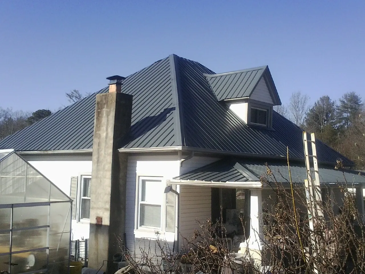 Dark blue standing seam metal roof on a white farmhouse with dormer — Slate & Tile Roof Repair by Roofing Brothers in Left Hand