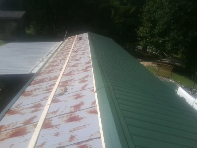 Old rusted panels beside newly installed green metal roofing — Wind Damage Roof Repair by Roofing Brothers in Left Hand