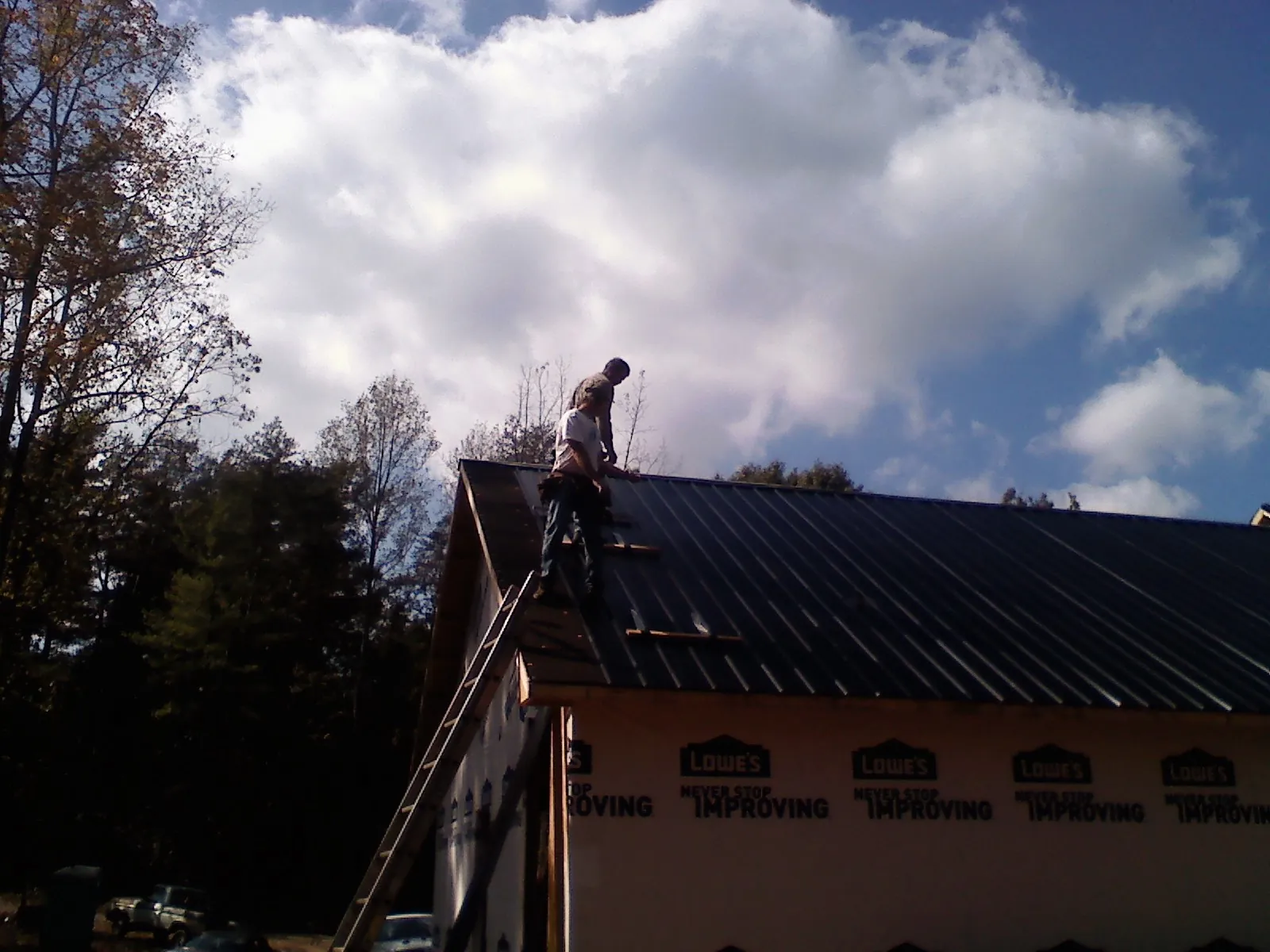 Roofer fastening dark metal panels high against a cloudy sky, from a Roof Inspection job in Left Hand