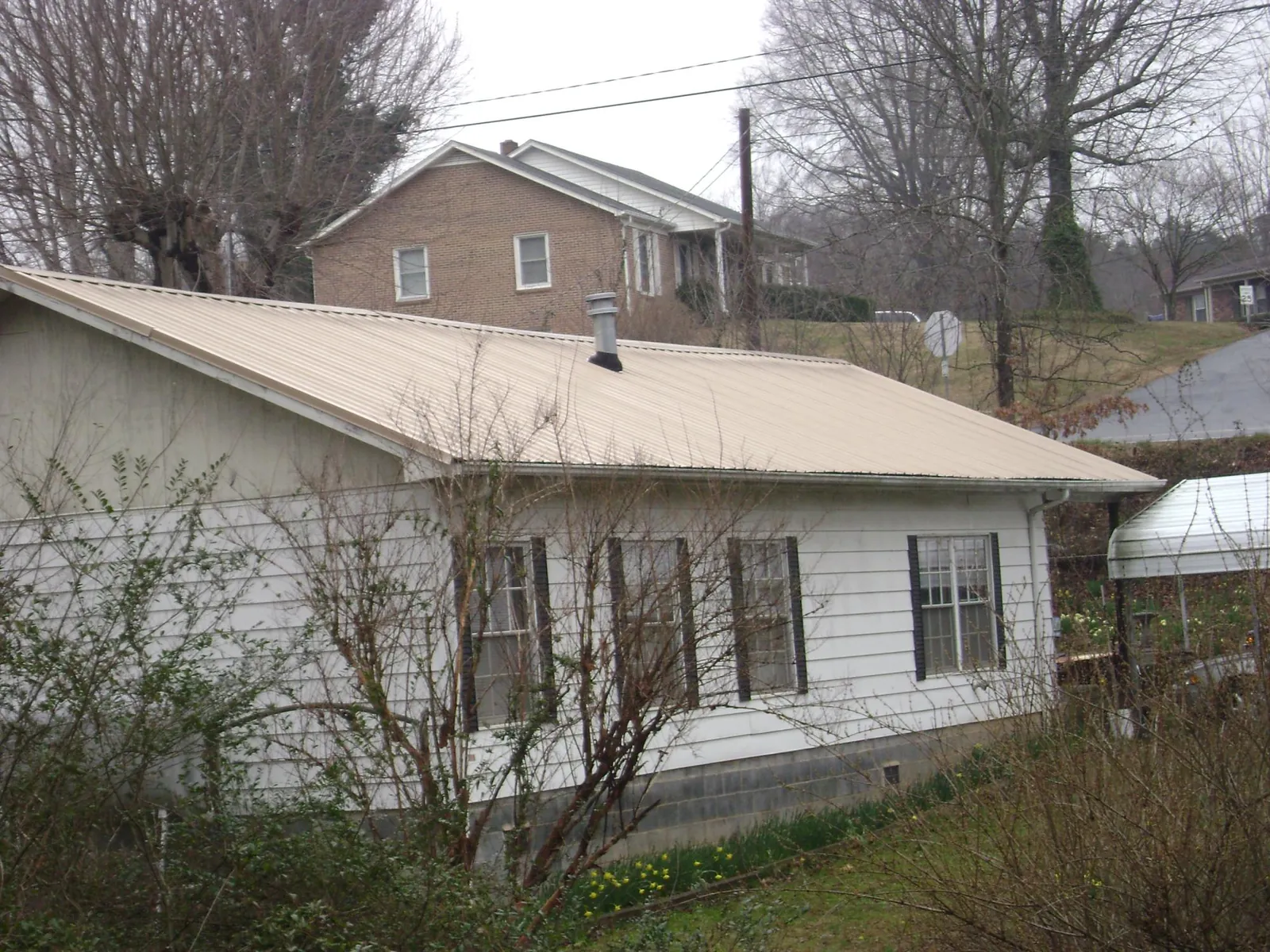 Tan metal roof on a white sided house set into a hillside — Commercial Roofing by Roofing Brothers in Left Hand