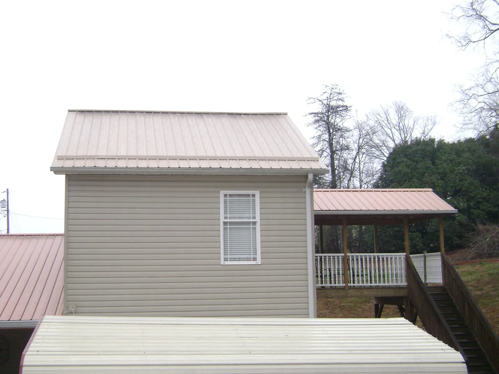 Tan metal roofs on a two story addition and attached porch, from a Roof Replacement job in Left Hand